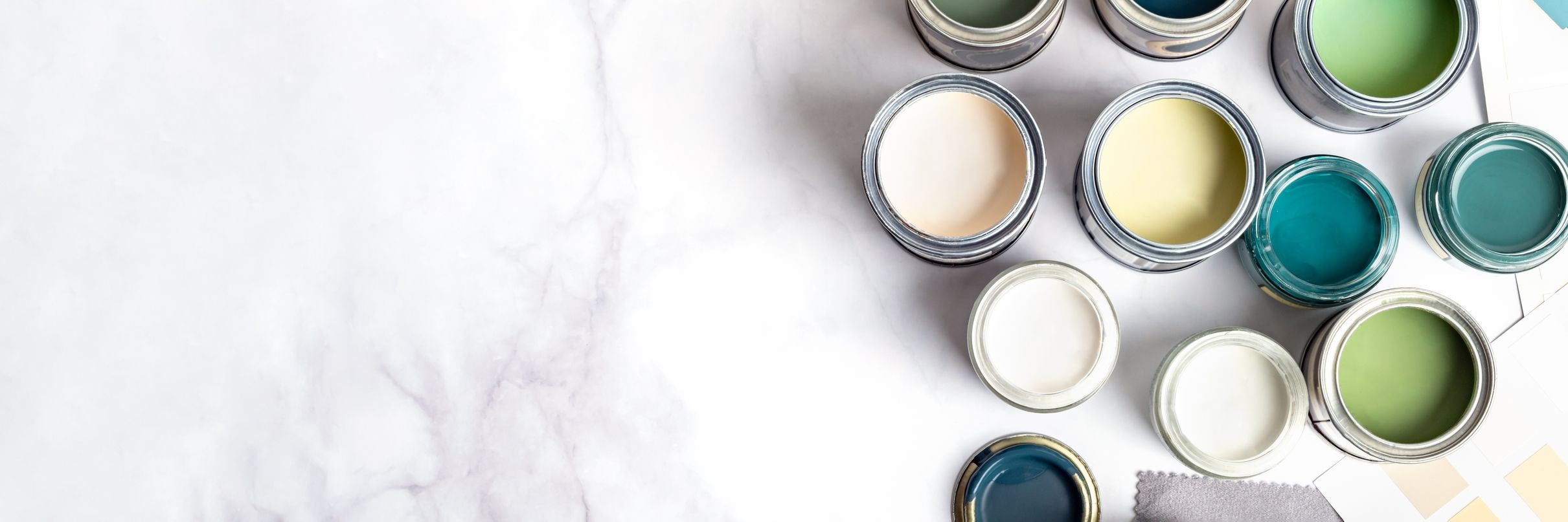 Mehrere Farbdosen mit verschiedenen Farben wie Grün, Blau, Creme und Weiß auf weißem Marmor-Untergrund angeordnet